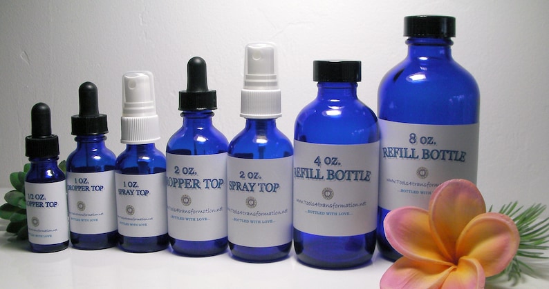 May include: An assortment of cobalt blue glass bottles with various tops, including droppers and sprayers. Sizes range from 1/2 oz to 8 oz, each labeled with white stickers. A tropical flower and greenery are in the foreground.