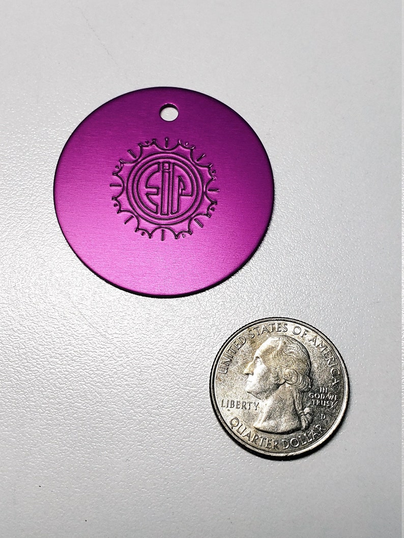 May include: A round, purple metal tag with a hole at the top. The tag has a circular design with the letters "SIP" inside.