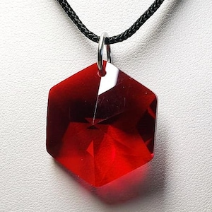 May include: A red gemstone pendant necklace with a black cord. The pendant is a faceted hexagon shape.