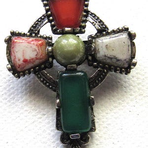 Può includere: Spilla a forma di croce color argento con pietre preziose colorate. La spilla presenta una disposizione di pietre rosse, bianche, verdi e grigie. Le pietre sono incastonate in una cornice metallica decorativa e strutturata. Il design a croce è un gioiello classico.