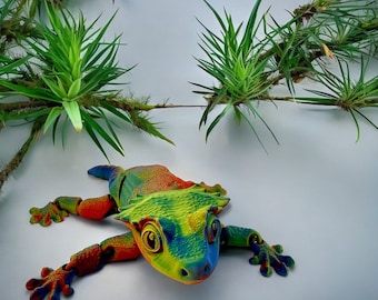 May include: A colorful, 3D printed gecko with a textured, bumpy surface. The gecko is green, blue, yellow, and red.