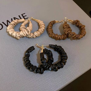 May include: Three pairs of hoop earrings with a gathered fabric design. The earrings are in beige, brown, and black.