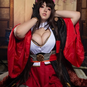 Peut inclure: Une femme vêtue d'un costume rouge et noir avec des oreilles de chat, posant les mains sur la tête. Elle porte une chemise blanche à col bas, une jupe rouge et une ceinture noire avec une boucle dorée. Le costume est décoré d'accents dorés.