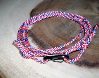 May include: Red, white, and blue paracord with a black metal clip. The paracord is coiled and tied in a knot.