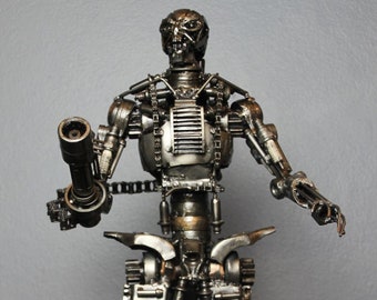 May include: A metal sculpture of a robot, made from recycled metal parts, with a gun in its right hand. The sculpture is standing on a black surface. The text "Metal Art Phuket" and "Facebook: Metal Art Phuket Etsy: btsteelart" is visible on the sculpture.