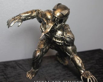 May include: A gold metal sculpture of Venom, a Marvel Comics character, in a crouching pose with its tongue extended. The sculpture is made of welded metal pieces and has a detailed, textured surface. The sculpture is signed "METAL ART PHUKET SHOP".