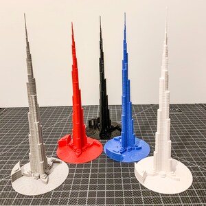 May include: Five 3D printed models of the Burj Khalifa skyscraper in different colours: grey, red, black, blue, and white.
