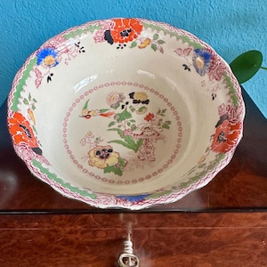 May include: A cream-colored, antique ceramic bowl with a scalloped edge. The bowl features a floral and bird design in red, orange, yellow, blue, and green. The rim has a green border with a red and white patterned edge.