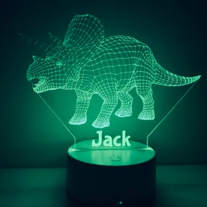 K&ouml;nnte beinhalten: Ein gr&uuml;nes, 3D-gedrucktes Dinosaurier-Nachtlicht mit dem Namen "Jack" darunter. Das Licht befindet sich auf einem wei&szlig;en Sockel mit einem Ein-/Ausschalter.