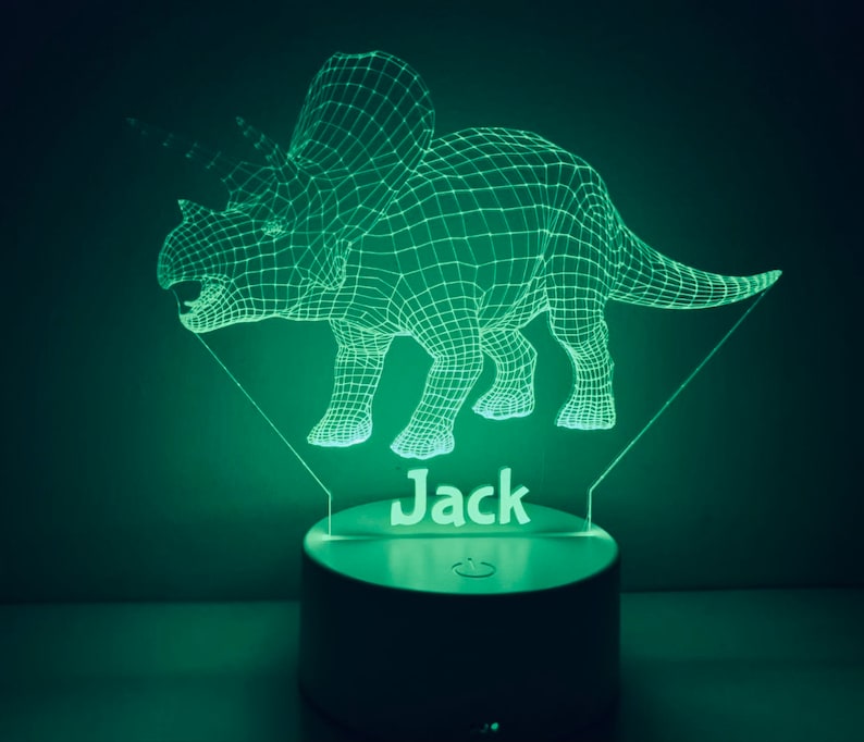 K&ouml;nnte beinhalten: Ein gr&uuml;nes, 3D-gedrucktes Dinosaurier-Nachtlicht mit dem Namen "Jack" darunter. Das Licht befindet sich auf einem wei&szlig;en Sockel mit einem Ein-/Ausschalter.