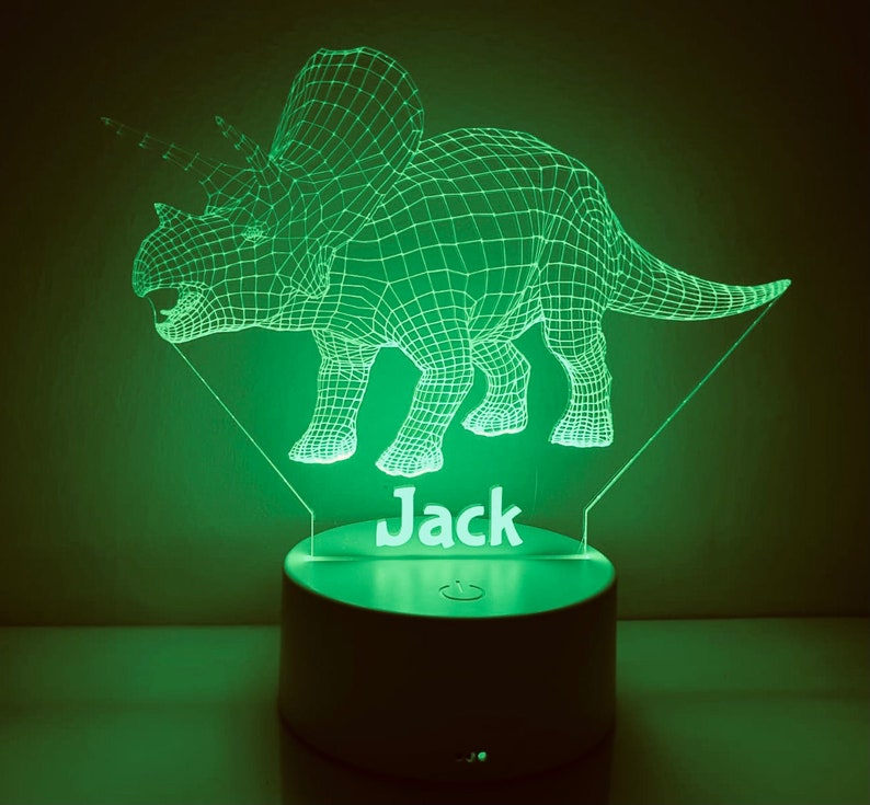 K&ouml;nnte beinhalten: Ein gr&uuml;nes, 3D-gedrucktes Nachtlicht in Form eines Triceratops-Dinosauriers mit dem Namen "Jack" darunter. Das Licht befindet sich auf einem wei&szlig;en Sockel mit einem Ein-/Ausschalter.