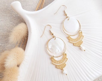 May include: A pair of gold earrings with white shell accents. The earrings feature a circular shell pendant with a gold wire hoop and a dangling gold charm with a pearl.