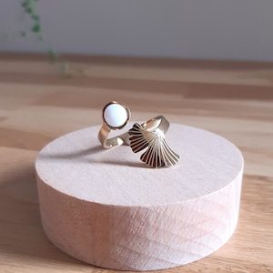 Peut inclure: Une bague en or avec une pierre ovale blanche et un motif en forme d'éventail. La bague est présentée sur un support en bois.