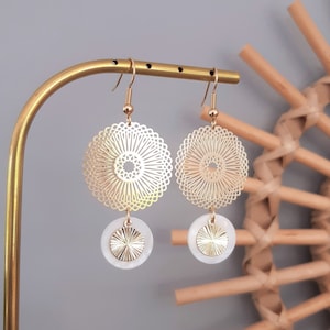 May include: Gold earrings with a delicate, circular design and a white, textured disc pendant.