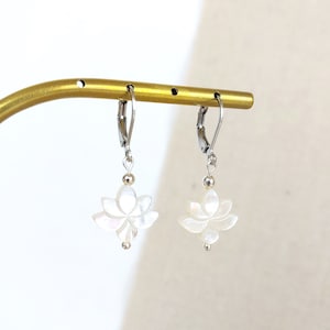 Peut inclure: Une paire de boucles d'oreilles en argent avec des breloques en forme de fleur de lotus en nacre blanche.