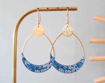 May include: Gold hoop earrings with a blue and white floral pattern on the bottom half of the hoop.