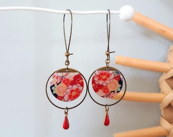 May include: A pair of dangle earrings with a red, pink and white floral design on a round, gold-toned metal base. The earrings have a red teardrop-shaped charm hanging from the bottom.