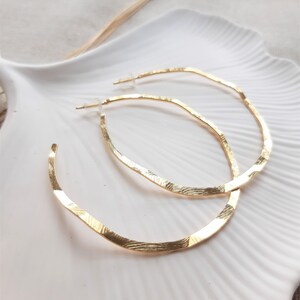 May include: A pair of gold hoop earrings with a textured finish. The hoops are large and have a slightly oval shape.