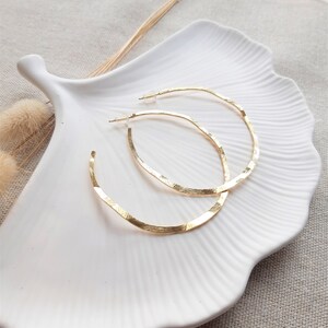 May include: A pair of gold hoop earrings with a textured finish. The earrings are displayed on a white ceramic plate.