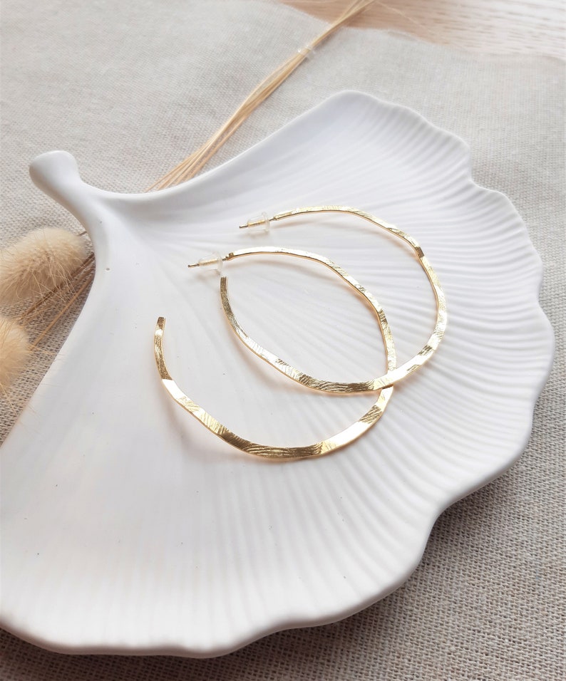 May include: A pair of gold hoop earrings with a textured finish. The earrings are displayed on a white ceramic plate.