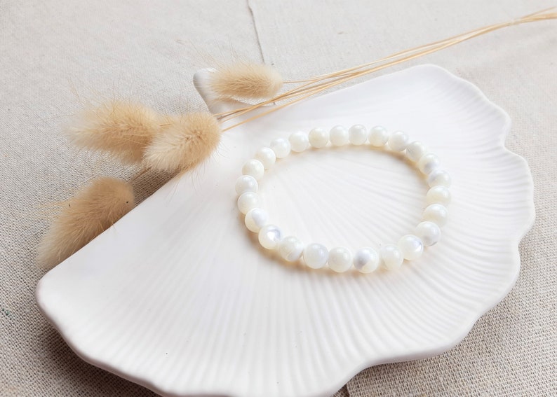K&ouml;nnte beinhalten: Ein wei&szlig;es Perlenarmband auf einem wei&szlig;en Keramikteller mit getrocknetem Pampasgras.
