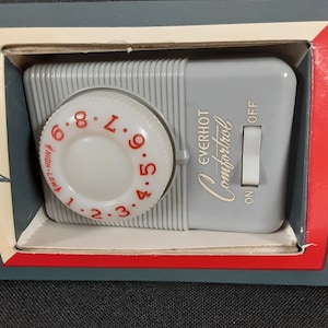 May include: A gray Everhot Comfortrol thermostat with a round dial that has numbers 1 through 9 and a red arrow. The dial also has the words "HIGH-LOW" and "7.8.9". The thermostat has an on/off switch with the words "ON" and "OFF" printed on it.