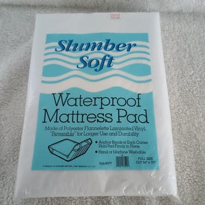 May include: White packaging for a Slumber Soft waterproof mattress pad. The packaging features blue waves and the text "Slumber Soft Waterproof Mattress Pad". The pad is made of polyester flannelette laminated vinyl and is reversible for longer use and durability. It has anchor bands at each corner to hold the pad firmly in place. The pad is hand or machine washable. The full size pad is 54 inches by 70 inches.