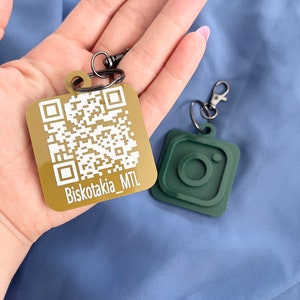 Peut inclure: Deux porte-clés, l'un avec un carré doré comportant un code QR et le texte "Biskotkia_MTL", et l'autre avec un logo Instagram vert.