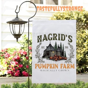 May include: A white garden flag with the text "Hagrid's Pumpkin Farm" in green and orange. The flag features an illustration of a stone cottage, pumpkins, and the text "Magically Grown."