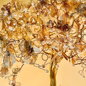 May include: A gold wire tree sculpture with white pearl beads and delicate gold flowers. The tree is crafted with intricate details and has a natural, organic feel.