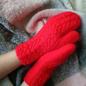 May include: A pair of bright red knitted mittens featuring a textured cable knit pattern on the back of the hand and a smooth knit palm. The mittens are crafted from a thick yarn and have a ribbed cuff at the wrist to ensure a secure fit.