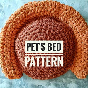 May include: A brown crocheted pet bed with a raised rim. The bed is made with thick yarn and has a soft, cozy texture. The text "PET'S BED PATTERN" is printed in white on the bed.