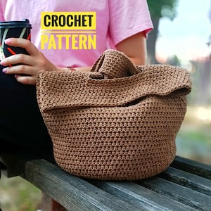 May include: A brown crochet tote bag with a folded top flap sits on a wooden bench. The bag is made with a tight stitch pattern. The words "CROCHET PATTERN" are in yellow block letters in the upper left corner.