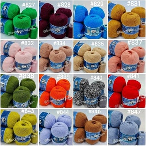 May include: A collection of sixteen sets of yarn balls in various solid colors and one speckled black and white pattern. Each set includes multiple balls of yarn wrapped with a blue label featuring a raccoon illustration and the text favorite_norka_yarn.