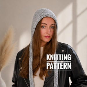 Puede incluir: Un gorro tejido de color gris claro con lazos laterales largos, que presenta un borde texturizado a lo largo de la parte frontal. El texto KNITTING PATTERN aparece en letras blancas mayúsculas en el centro, indicando una guía.