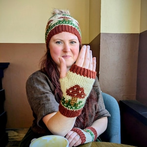 May include: A knitted hat and fingerless gloves set. The hat has a brown, green, and cream pattern with a faux fur pom-pom. The fingerless gloves feature a mushroom design. The set is made of a soft, warm material, perfect for cold weather.