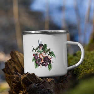 May include: White enamel camping mug with a colorful illustration of a fairy sitting on a blackberry bush. The fairy is wearing a green shirt and brown shorts.