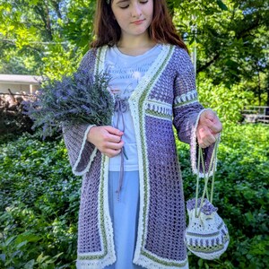 May include: A handmade crochet ensemble in shades of purple, white, and green. The outfit includes a long cardigan, a small drawstring bag, and a matching headband. The cardigan features a delicate open weave and trim. The ensemble is perfect for a bohemian or cottagecore aesthetic.