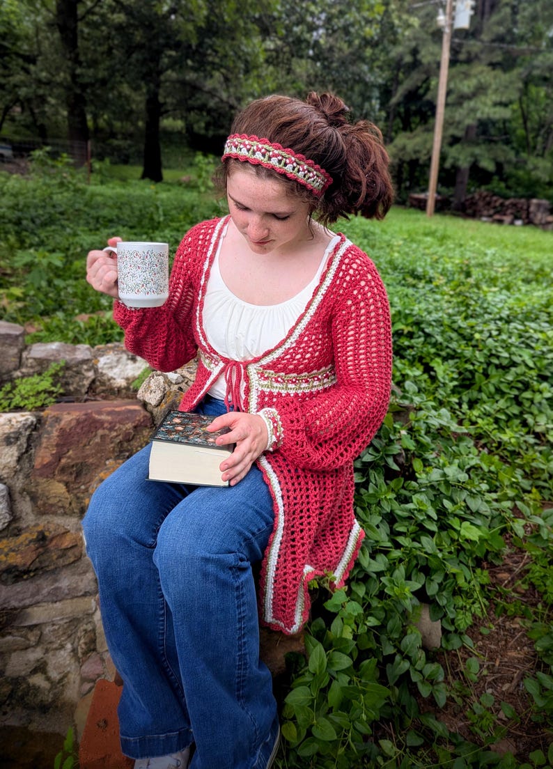 May include: A red crochet cardigan with white trim, and a matching headband. The cardigan is worn over a white top and blue jeans. A floral-patterned mug and a book are also visible.