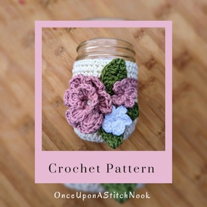 May include: Crochet pattern for a mason jar cozy with pink, white, and green flowers. The pattern is called "Once Upon A Stitch Nook".