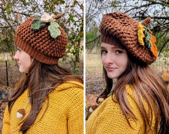 May include: A brown crochet hat with a leaf and acorn design. The hat is a warm brown color and features a textured pattern. The leaves are green, orange, and cream. The person is wearing a yellow sweater.