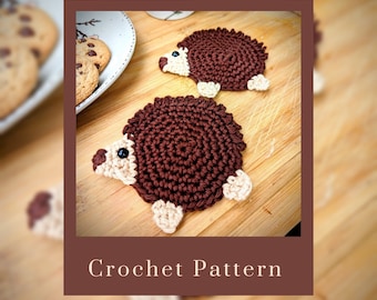 May include: Two brown crocheted hedgehog coasters with white accents. The coasters are on a wooden surface. Crochet Pattern OnceUponAStitchNook