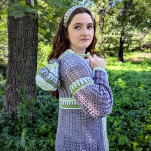 May include: A lavender crochet duster with a matching headband. The duster features green and white trim on the sleeves, waist, and hood. The open weave design is visible throughout the garment. The headband has a similar pattern to the trim.