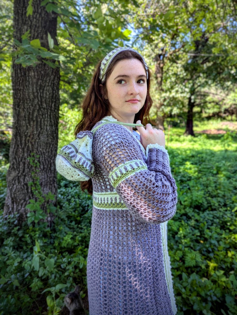 May include: A lavender crochet duster with a matching headband. The duster features green and white trim on the sleeves, waist, and hood. The open weave design is visible throughout the garment. The headband has a similar pattern to the trim.