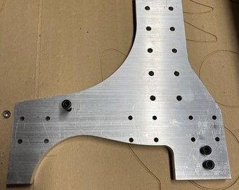 May include: A silver metal bracket with multiple holes and two black screws. The bracket is on a brown surface.