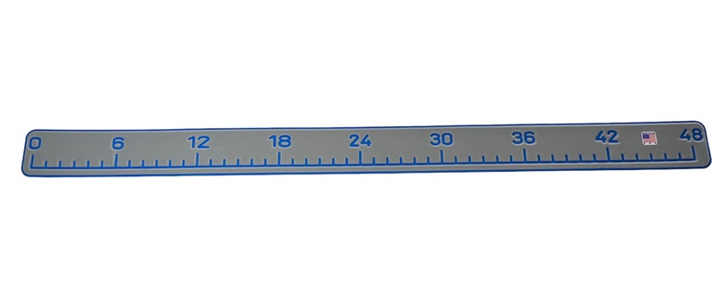 Pu&ograve; includere: Un righello piatto e rettangolare grigio con angoli arrotondati, caratterizzato da segni e numeri blu stampati da 0 a 48 pollici. Il righello ha un bordo blu e una piccola icona della bandiera americana vicino al segno dei 48 pollici.