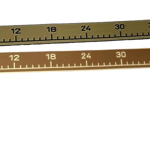 Pu&ograve; includere: Due nastri di misurazione flessibili, uno verde oliva e uno marrone, contrassegnati con incrementi numerici neri o bianchi da 0 a 122 cm. Entrambi i nastri presentano un piccolo logo rettangolare sul lato destro e una forma curva e allungata.