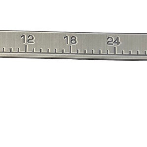 May include: A silver ruler with black markings and numbers from 0 to 36. The ruler has a small American flag printed on it.