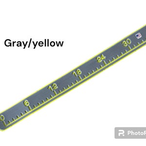 May include: Gray and yellow measuring tape with markings in inches from 0 to 36. The tape is made of metal and has a yellow border.