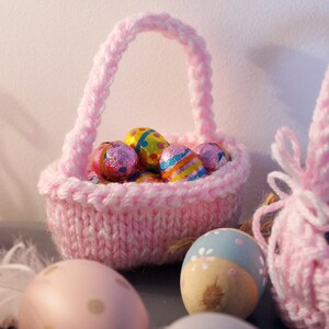 May include: Two pink knitted Easter baskets filled with colorful foil-wrapped chocolate eggs. The baskets have white yarn handles.